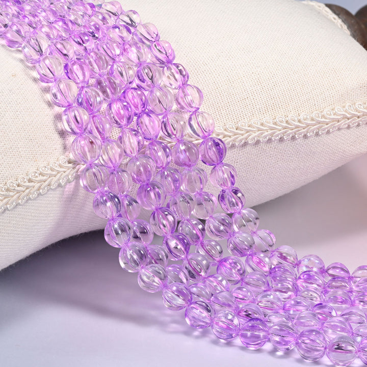 Clear purple pumpkin glass beads, 8mm fluted melon rounds, several strands draped over a white cushion.