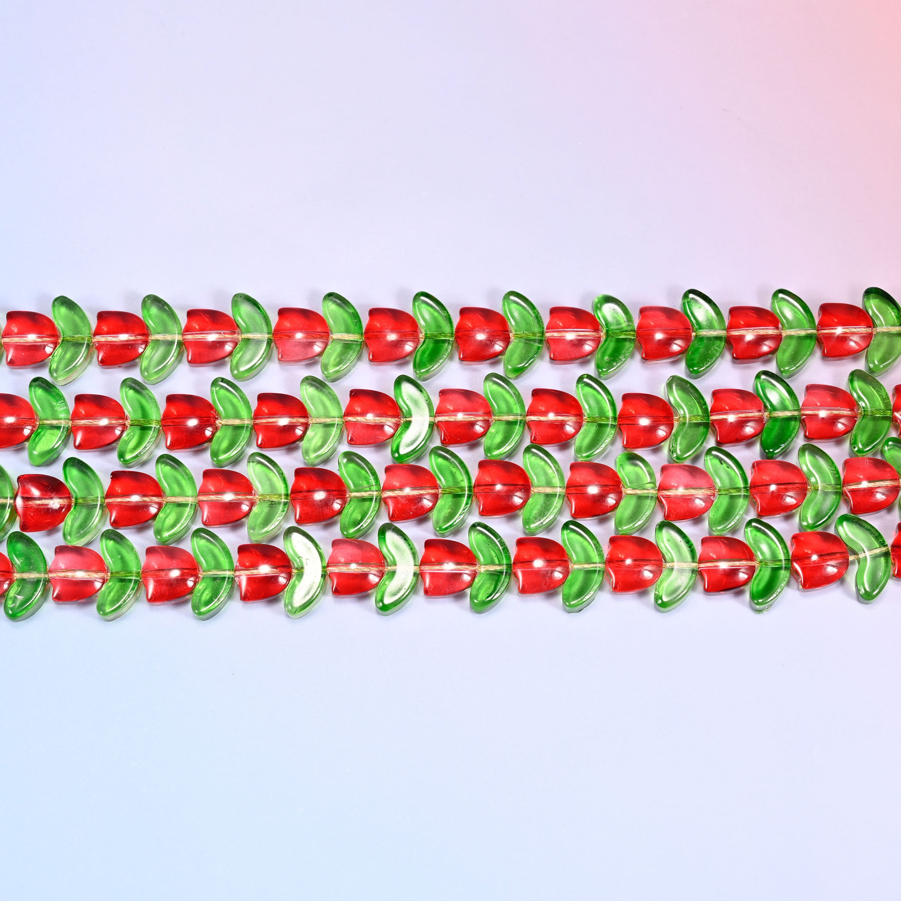 Close-up macro view of red tulip and green leaf glass beads in a dense repeating row pattern on a lavender and pink gradient background.