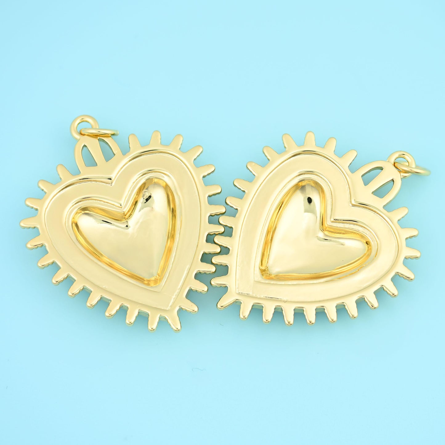 A full, puffed heart framed by a ring of radiating spikes, polished to a bright gold shine, with a bail ring at the top and…