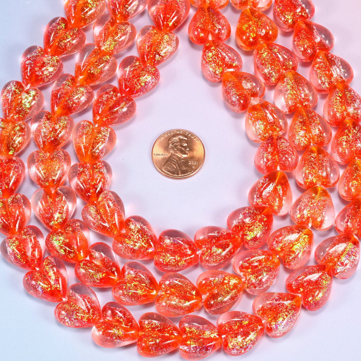 Warm coral-red transparent hearts, thick and glossy, shot through with golden iridescent glitter