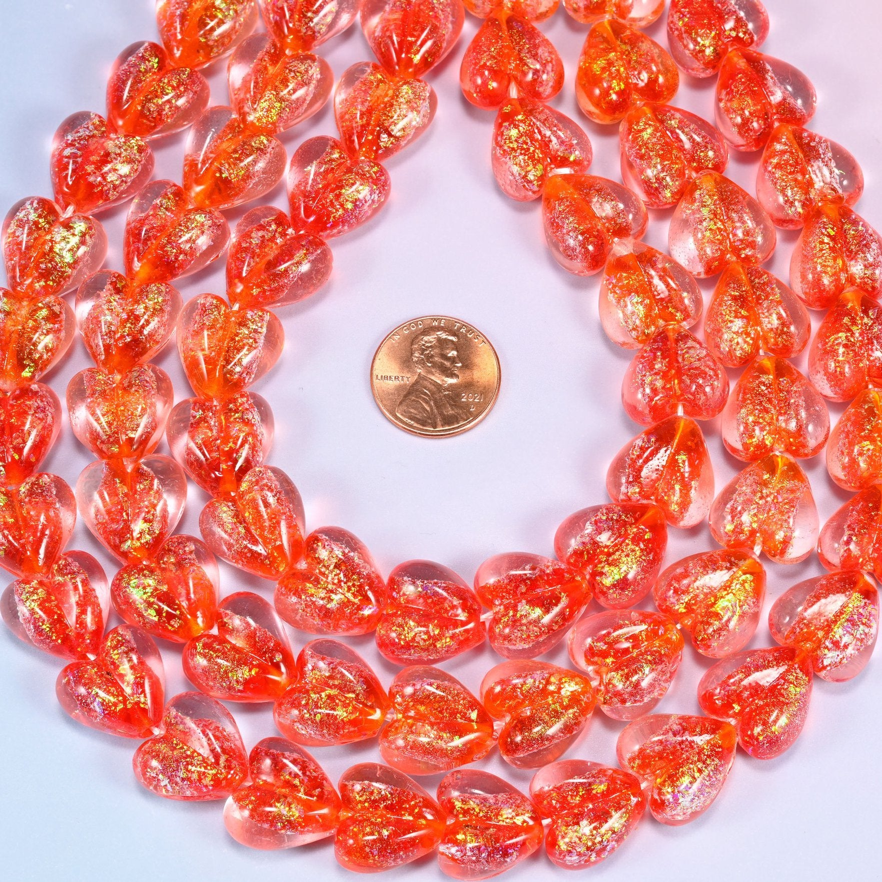 Warm coral-red transparent hearts, thick and glossy, shot through with golden iridescent glitter