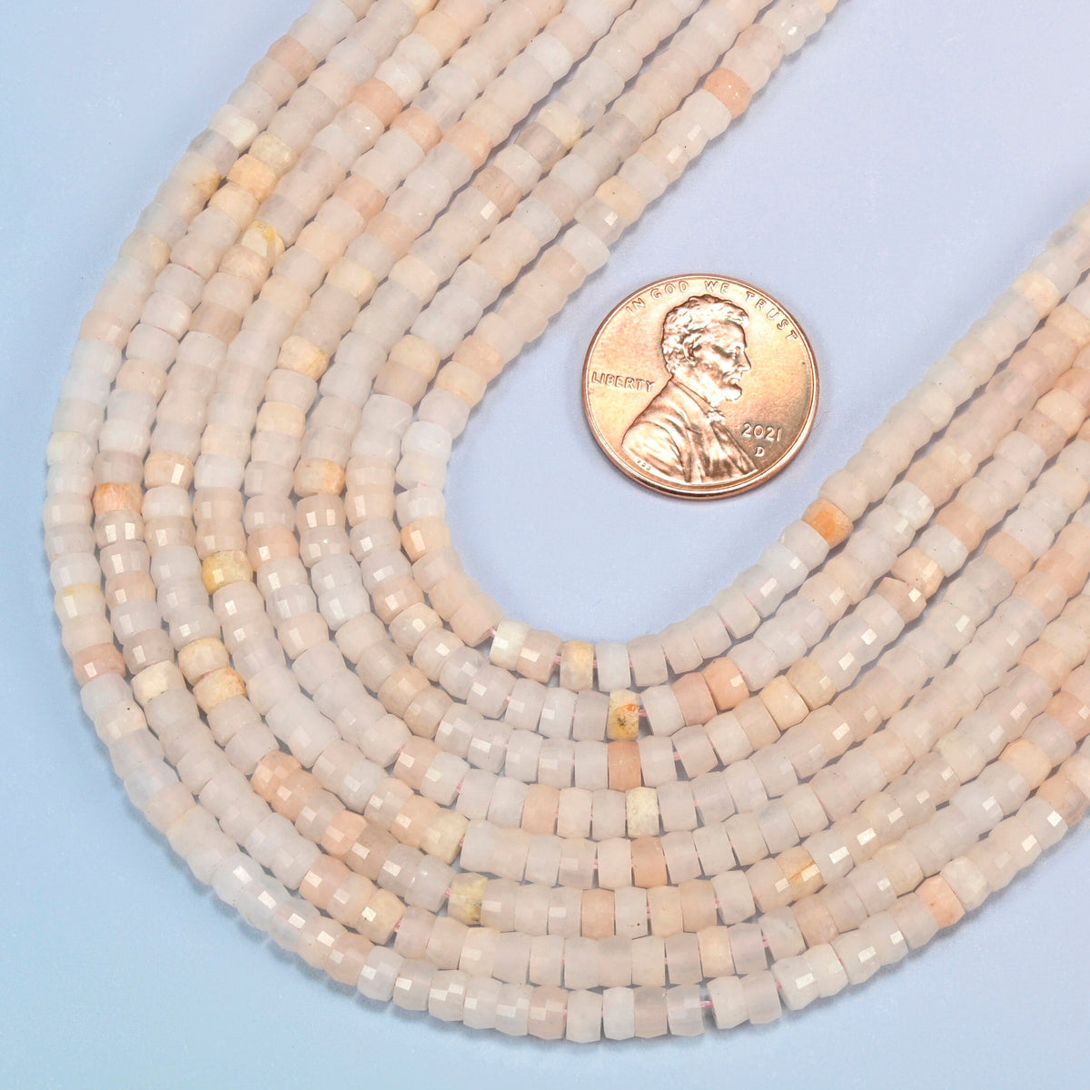 Close view of pink aventurine faceted heishi disc strands curving beside a US penny for scale