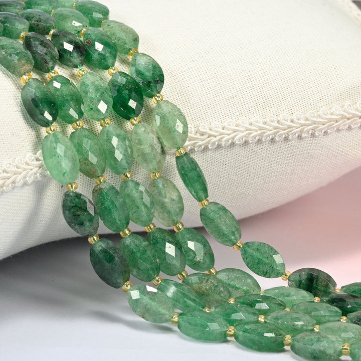 Green strawberry quartz faceted flat oval beads 9x14mm with small gold seed bead spacers, several strands draped over a white cushion