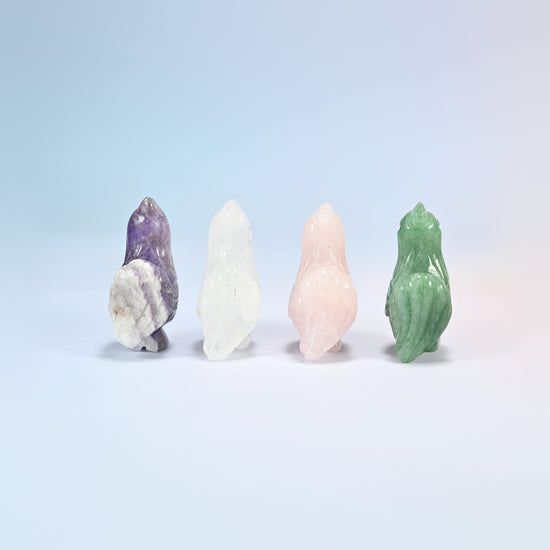Back view of four rooster crystal carvings in amethyst, clear quartz, rose quartz and green aventurine