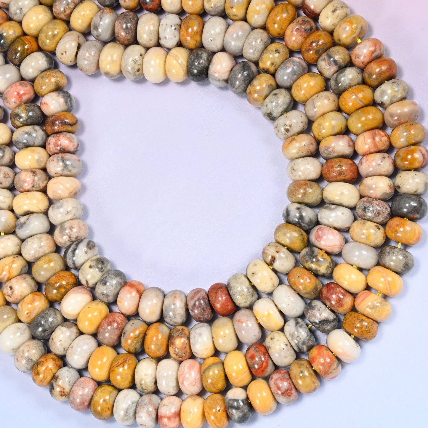 Rows of Crazy Agate rondelle beads laid straight on a lavender surface, showing the natural stone color variation.