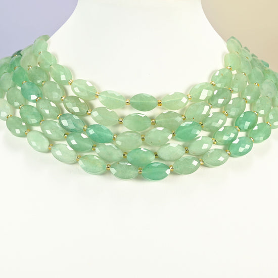 Green aventurine faceted flat oval strands arranged as a layered collar on a white display bust, mint green beads across the neck