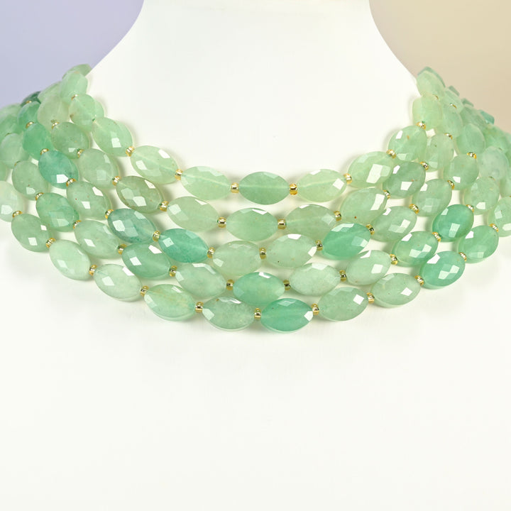 Green aventurine faceted flat oval strands arranged as a layered collar on a white display bust, mint green beads across the neck