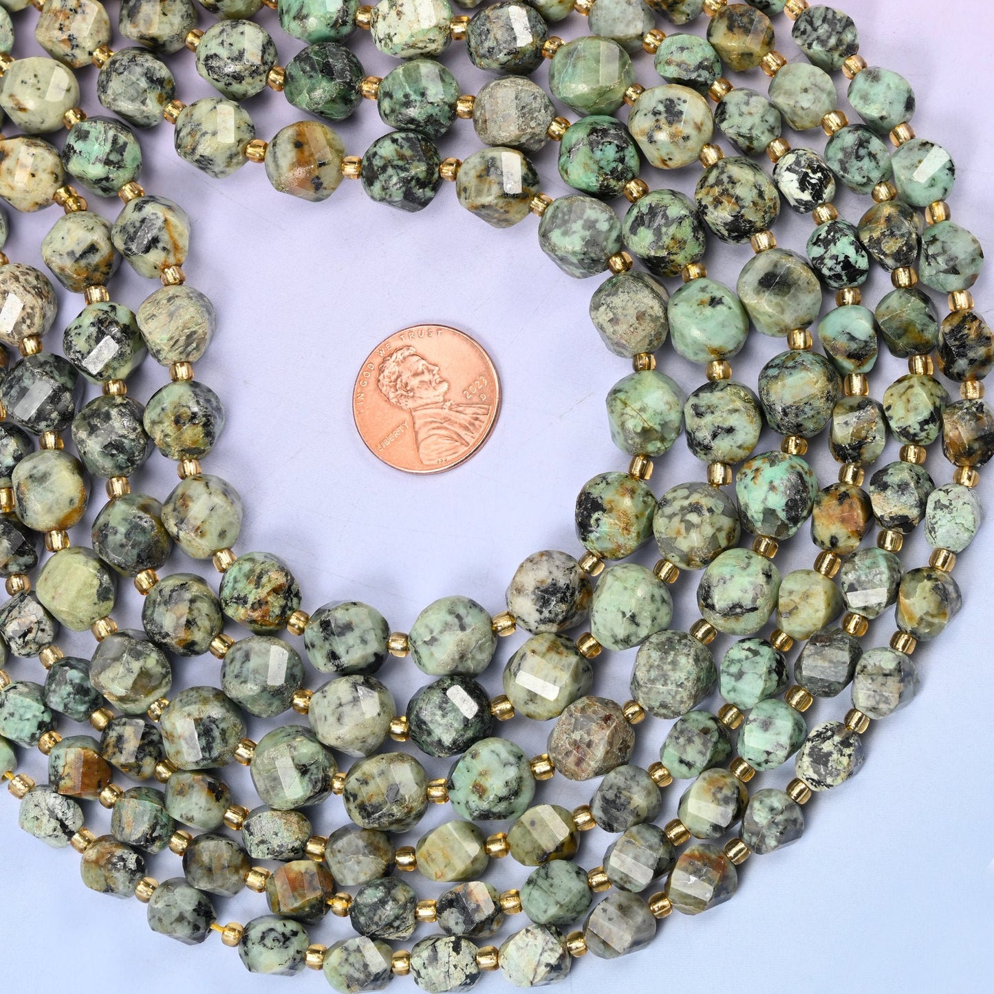 Soft sage and celadon green speckled and veined with black matrix, cut into a faceted spiral twist so the facets wind around the bead instead of sitting in straight rows