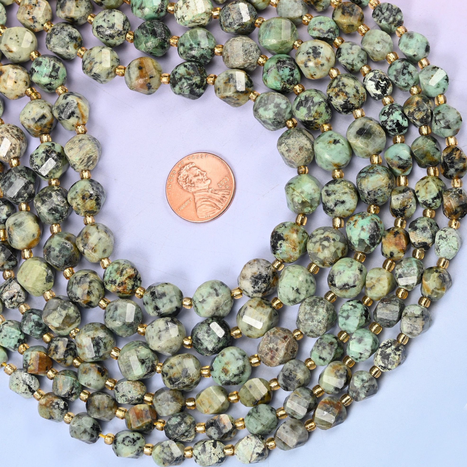Soft sage and celadon green speckled and veined with black matrix, cut into a faceted spiral twist so the facets wind around the bead instead of sitting in straight rows