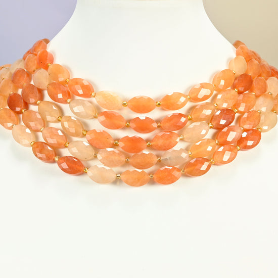 Red aventurine faceted flat oval strands arranged as a layered collar on a white display bust, peach and orange beads across the neck
