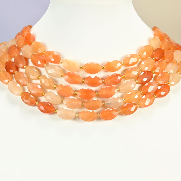 Red aventurine faceted flat oval strands arranged as a layered collar on a white display bust, peach and orange beads across the neck