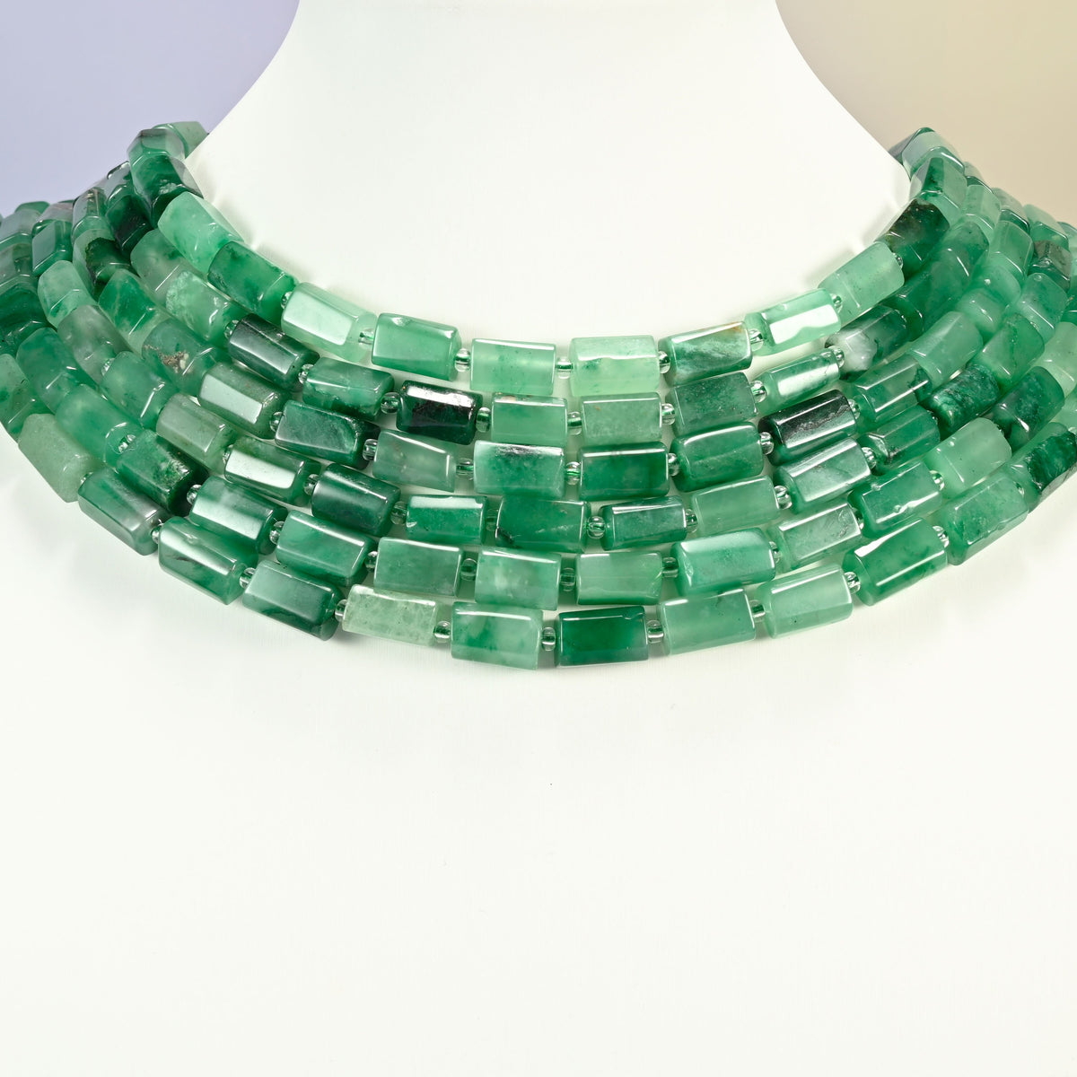 African jade faceted tube strands arranged as a layered collar on a white display bust, emerald and forest green beads across the neck