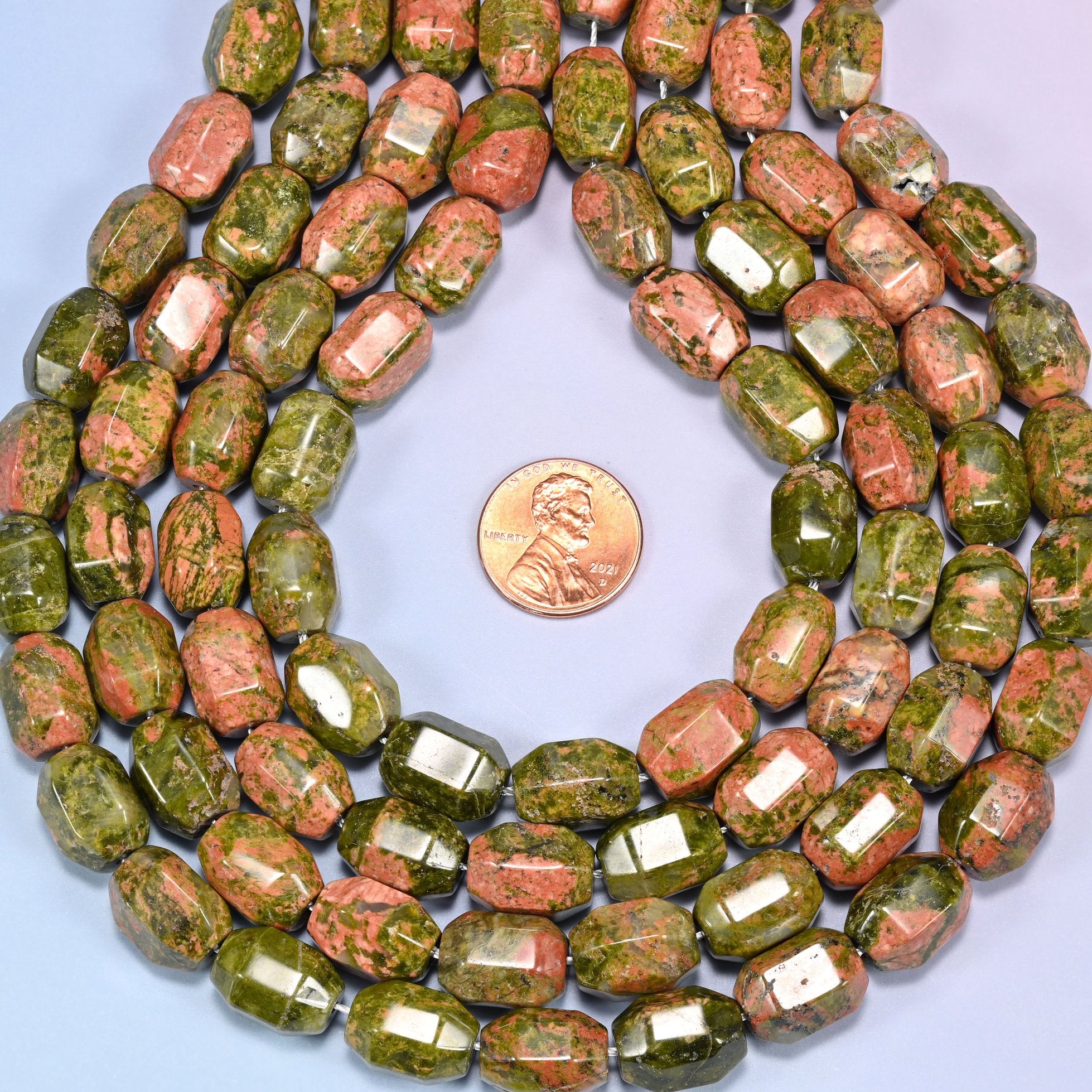 Wide circular coil of faceted Unakite barrel bead strands on a light blue background with a penny in the center for size comparison.