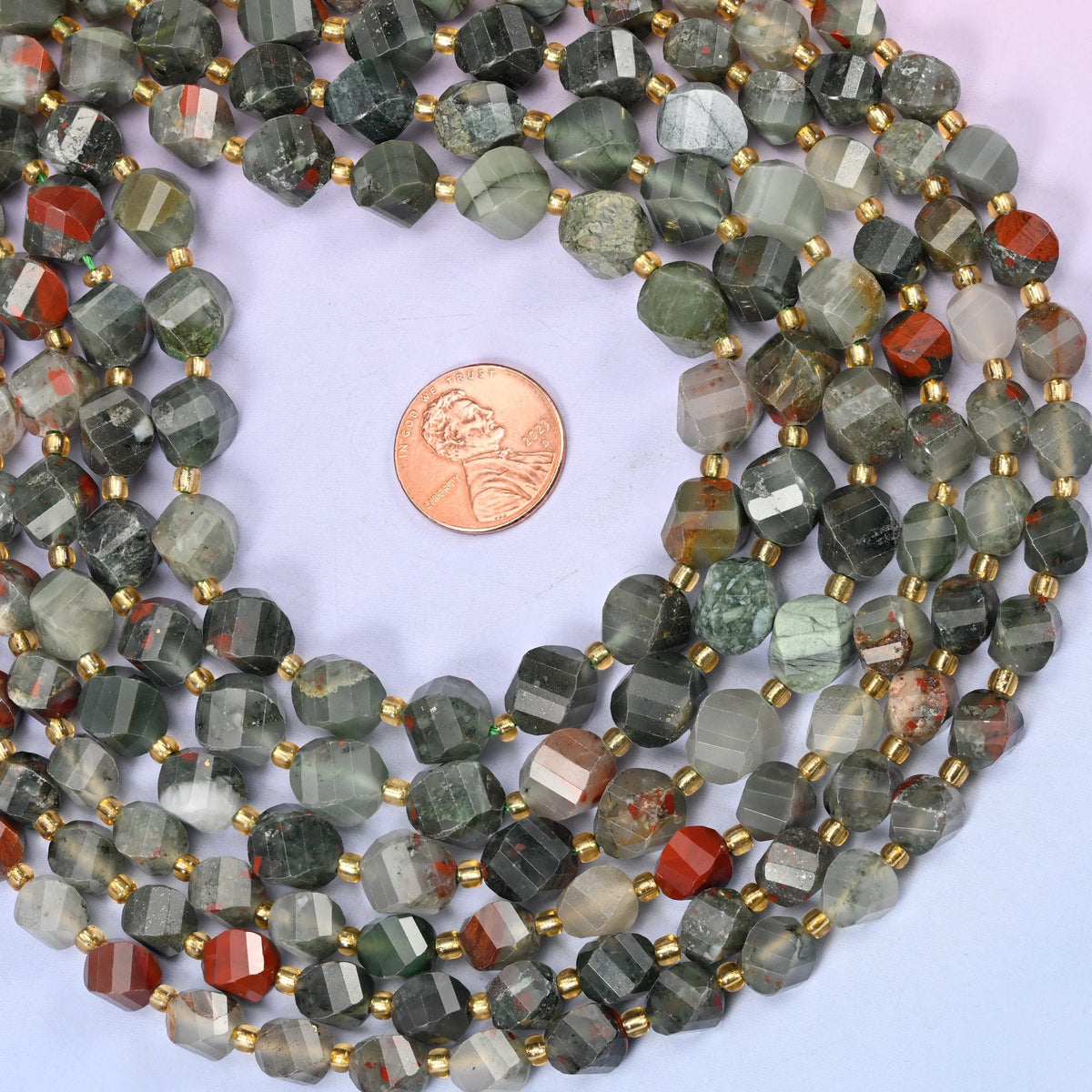 Sage and forest green stone clouded with pale grey and interrupted by patches of brick red, cut with facets that wind around the bead so each turn shows a different part of the pattern.
