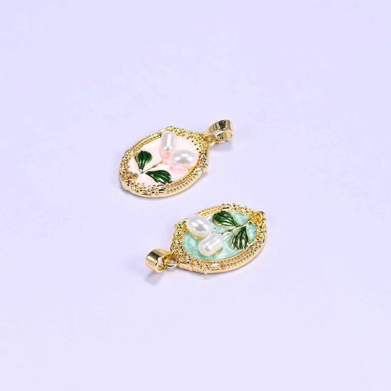 Enamel Oval Tulip Flower Pendants lying at angles on a soft lilac background, the peach oval above and the mint oval below.