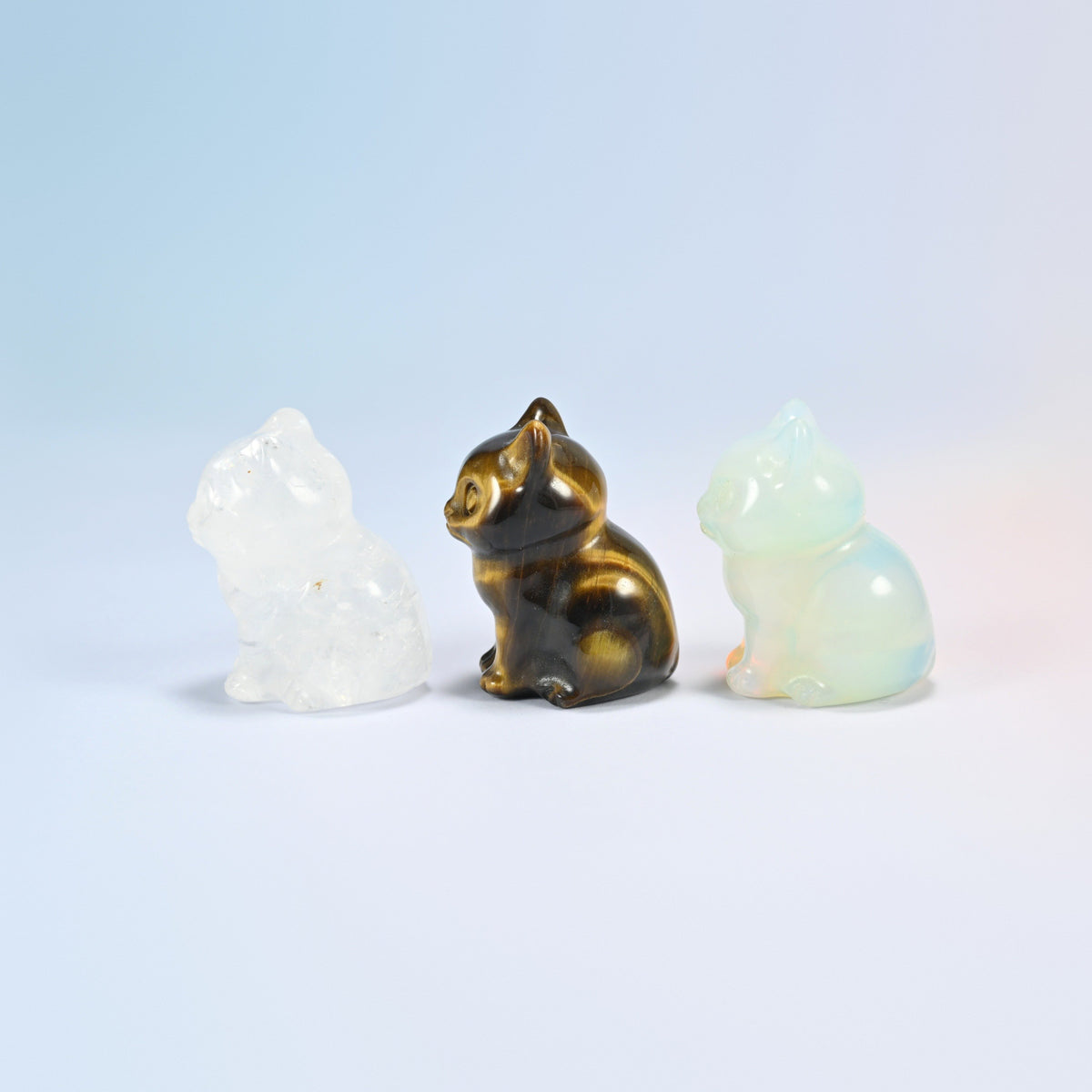 Side view of clear quartz, tiger eye and opalite sitting cat figurines showing the curled tail