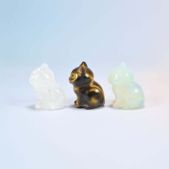 Side view of clear quartz, tiger eye and opalite sitting cat figurines showing the curled tail