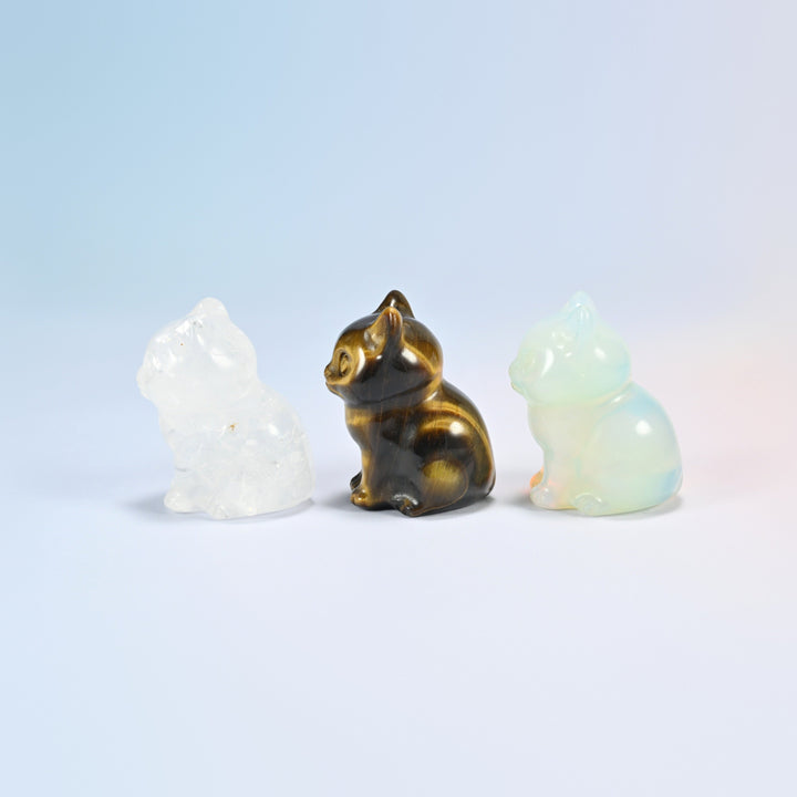 Side view of clear quartz, tiger eye and opalite sitting cat figurines showing the curled tail