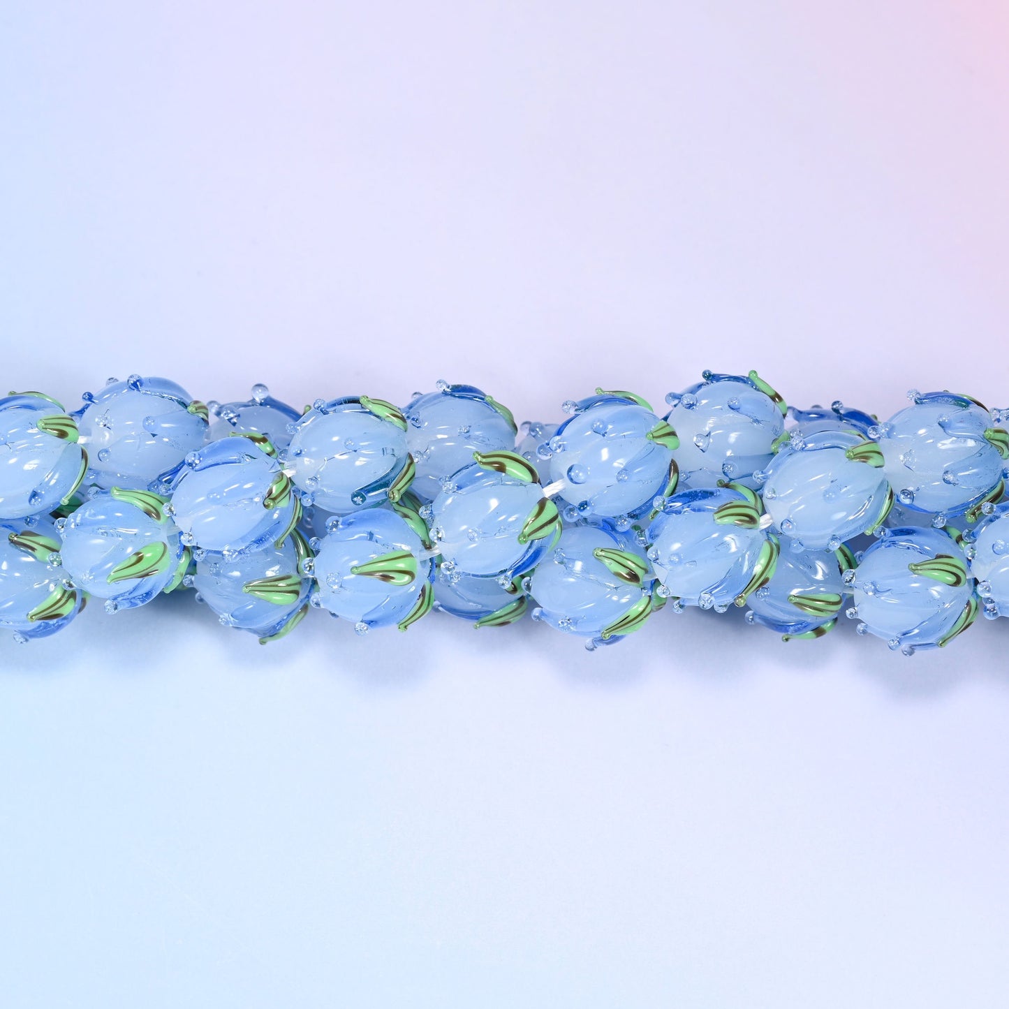 Blue tulip buds worked by hand at the lamp — closed petals sculpted into the glass and a green leaf detail wrapped at the base, so each bead reads as a small flower rather than a flower-shaped disc.