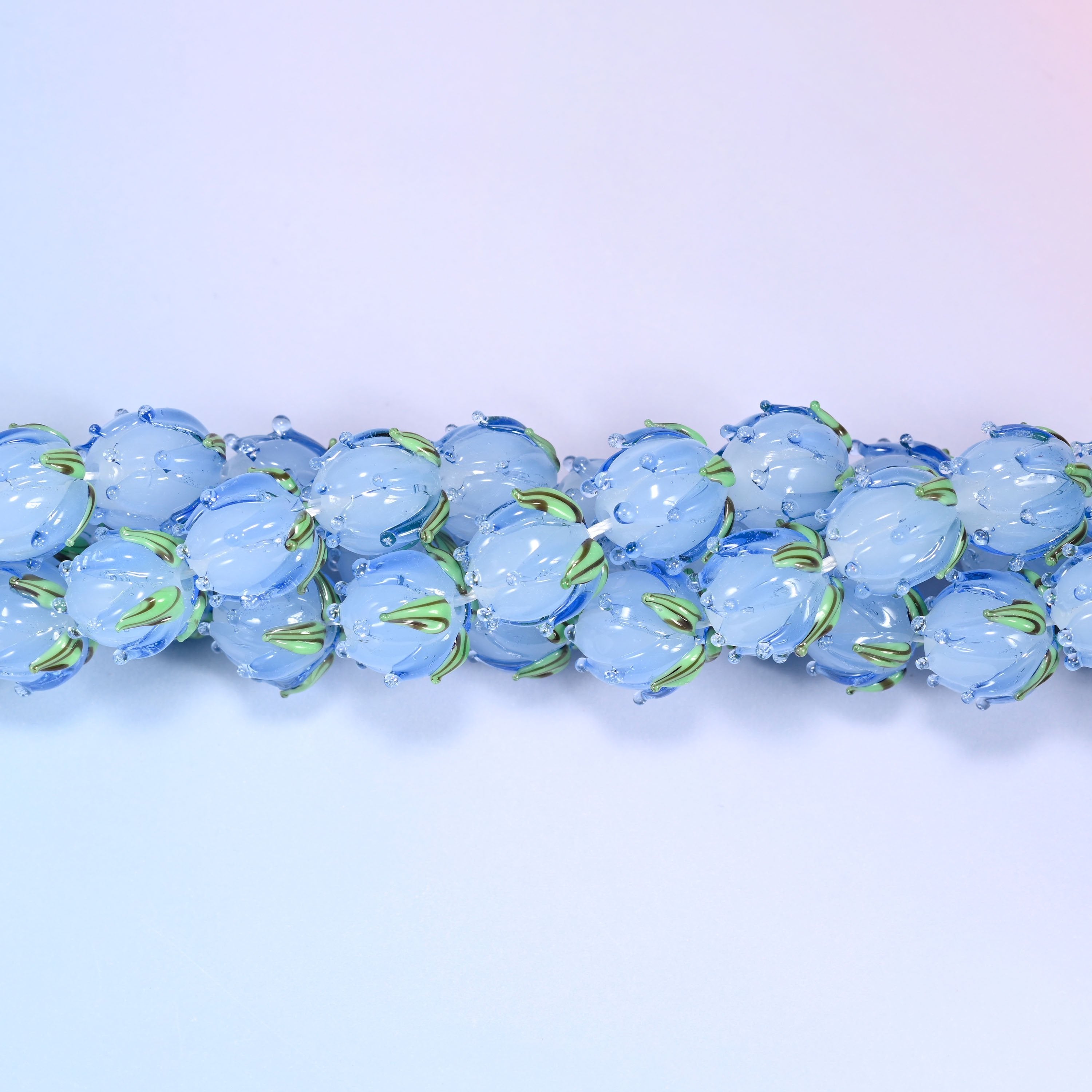 Blue tulip buds worked by hand at the lamp — closed petals sculpted into the glass and a green leaf detail wrapped at the base, so each bead reads as a small flower rather than a flower-shaped disc.