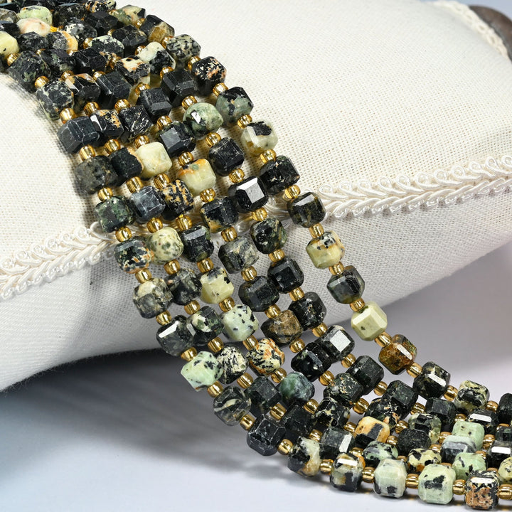 Old African howlite faceted cube beads 6mm with small gold spacer beads, several strands draped over a white cushion
