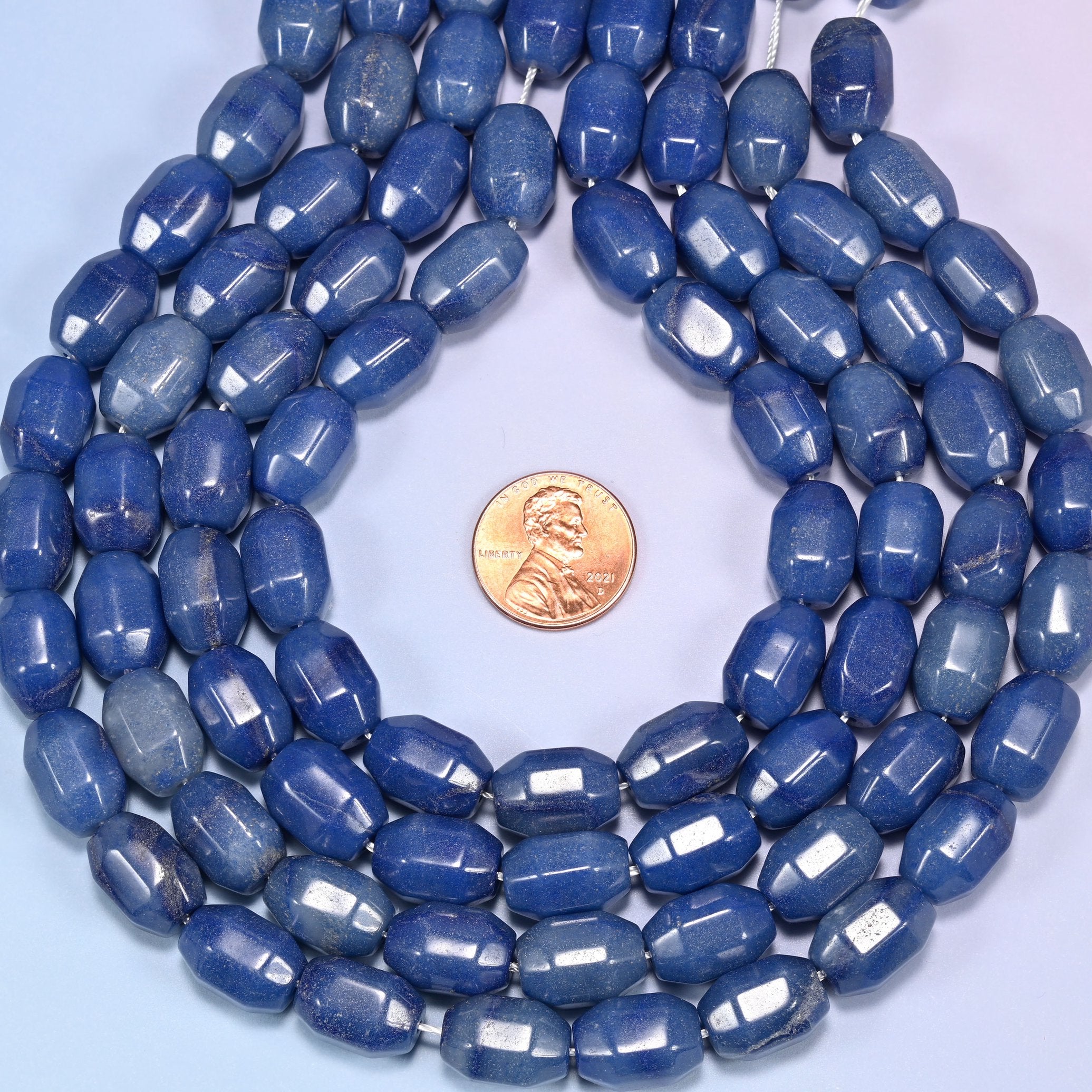 Wide circular coil of blue faceted Aventurine barrel bead strands forming a full wreath shape on a light blue background.