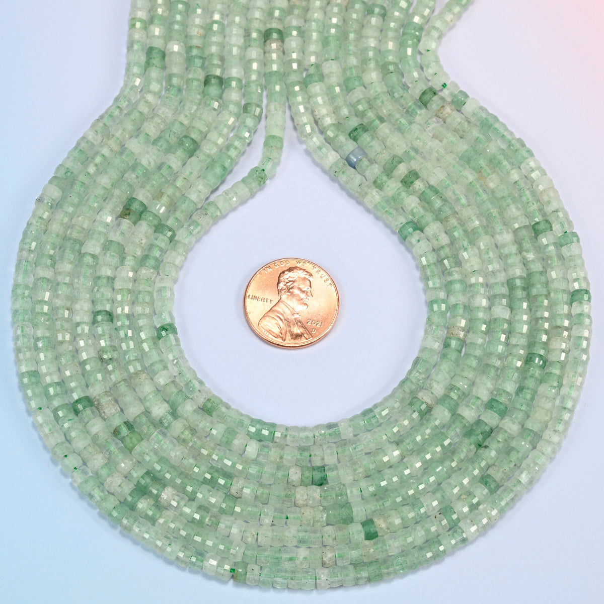 Green strawberry quartz faceted heishi disc strands formed into a teardrop loop around a US penny for scale