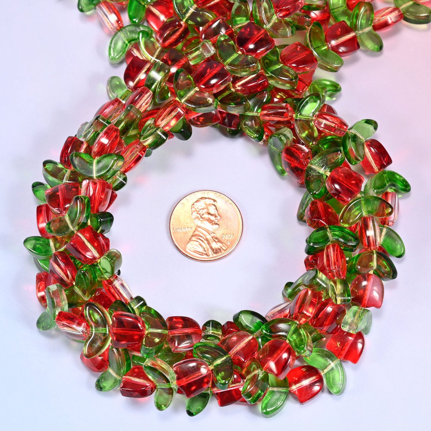 Bundled circular coil of tulip and leaf glass bead strands on a lavender background with a penny placed at the center for scale.