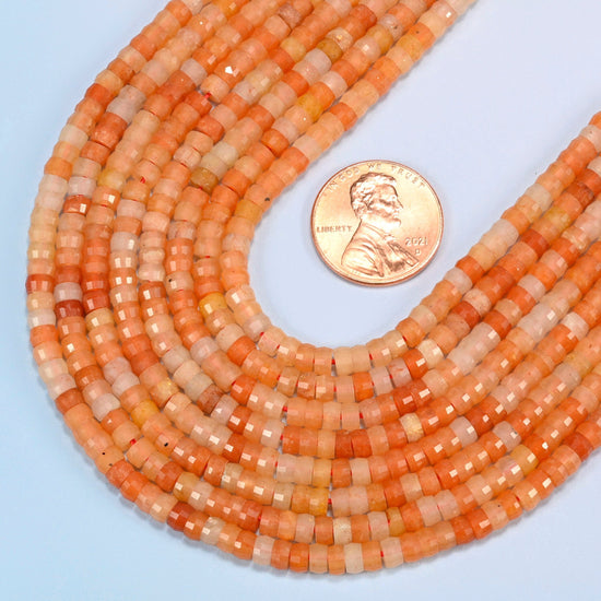 Close view of red aventurine faceted heishi disc strands curving beside a US penny for scale