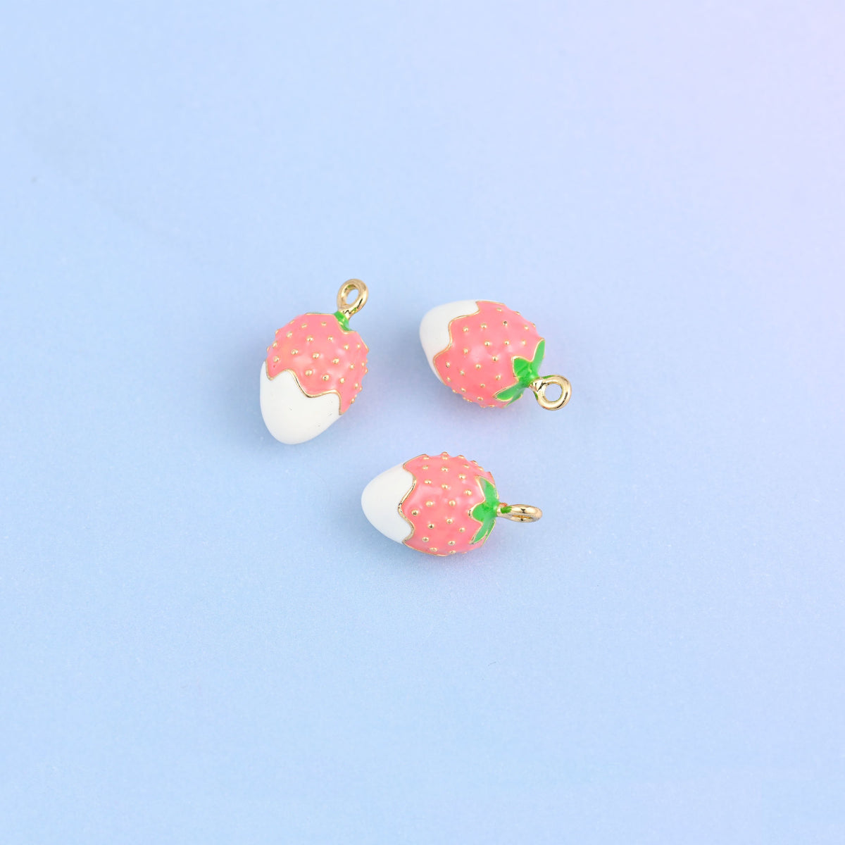 Three strawberry charms dipped in white enamel, red berry above with white seed dots.