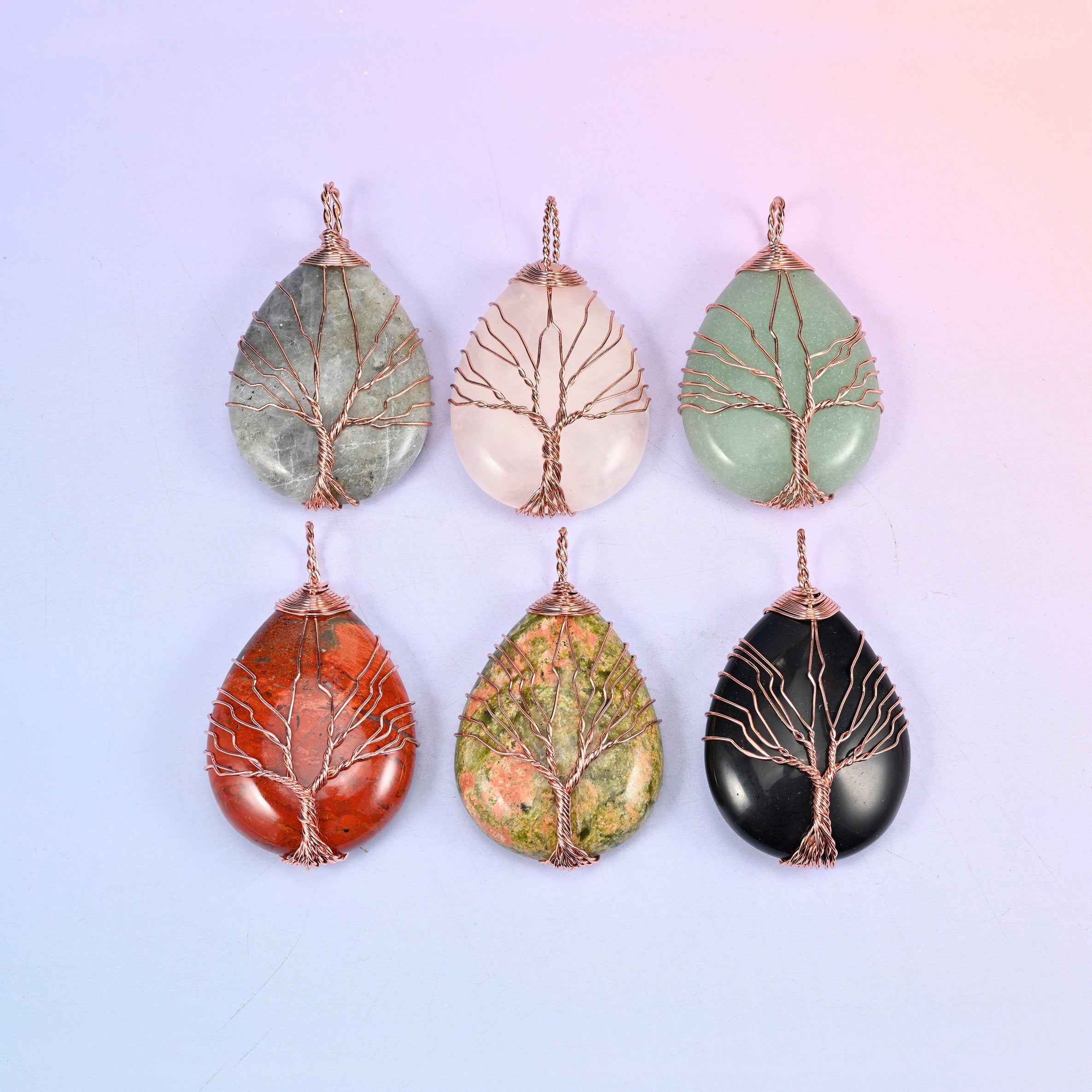 Six stone options of the Teardrop Crystal Pendant with Copper Wired Tree laid out together: moss agate, rose quartz, aventurine, red jasper, unakite and obsidian.