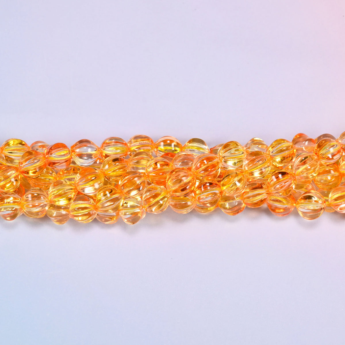 Yellow gold pumpkin glass beads, 8mm melon rounds, strands laid in a gentle wave straight across the frame.