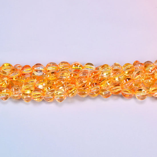 Yellow gold pumpkin glass beads, 8mm melon rounds, strands laid in a gentle wave straight across the frame.