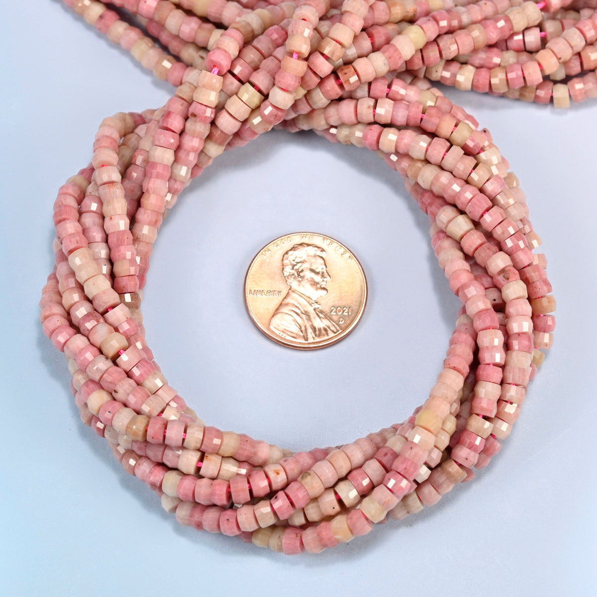 Pink rhodonite faceted heishi disc beads 2x4mm coiled in a loop around a US penny for scale, close-up of the faceted disc shape