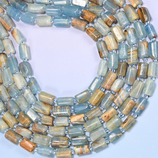 Circular coil of faceted Blue Calcite tube bead strands on a lavender background with a penny in the center for size comparison.