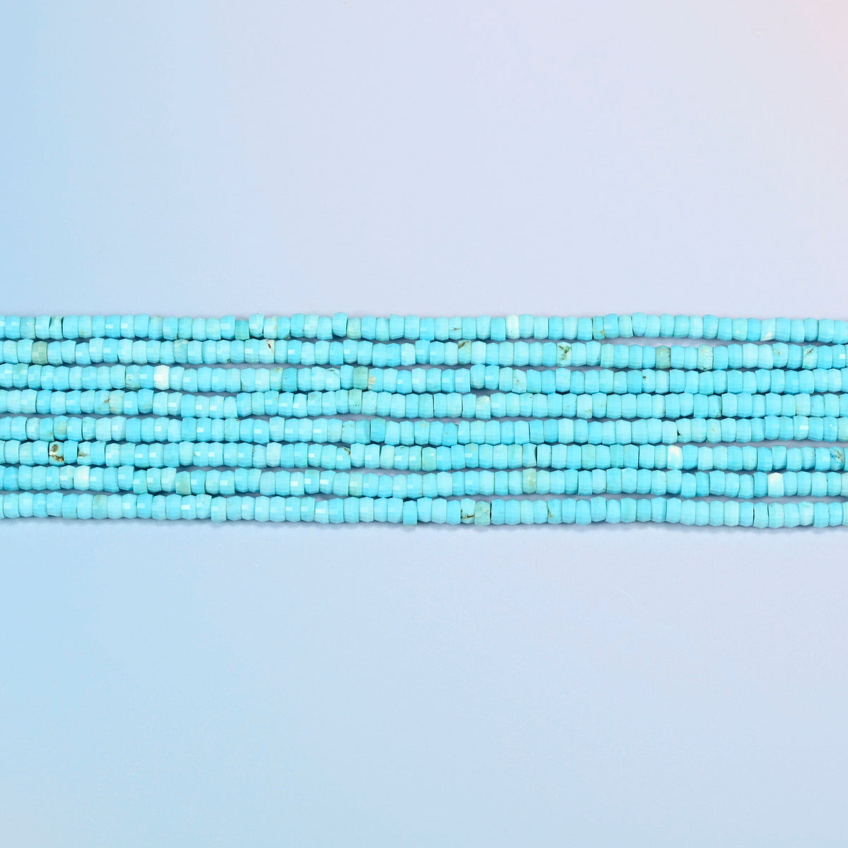 Several strands of dyed blue howlite faceted heishi disc beads laid in straight rows