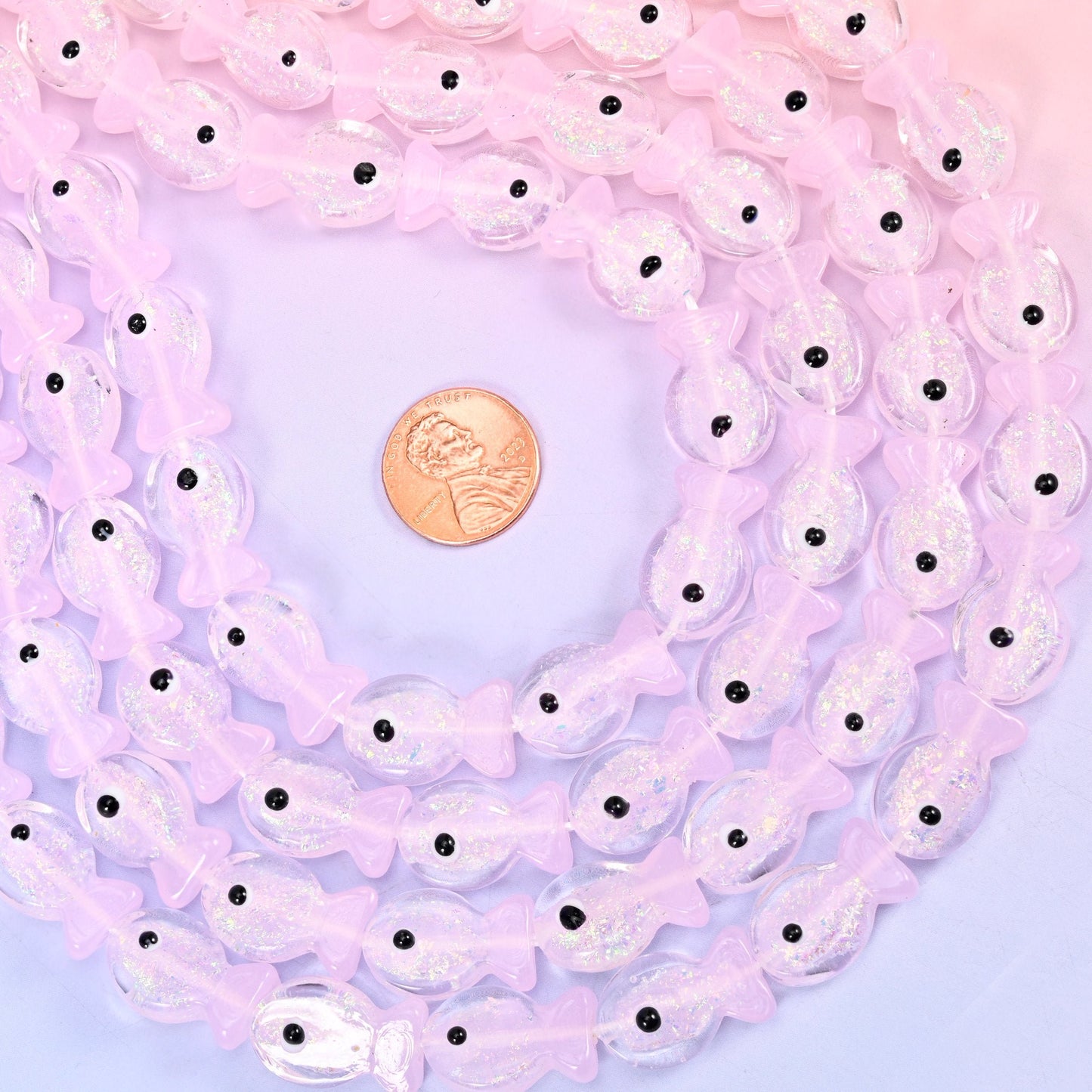Iridescent Pink Fish Glass Beads — little fish moulded in pale petal-pink glass with a pearly iridescent sheen across the body, a raised tail and fin, and a single black dot for the eye.