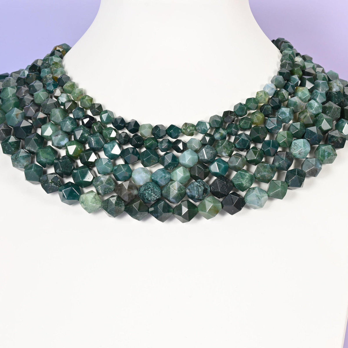 Moss Agate star cut beads looped around a white neck form, several strands sitting together as a collar