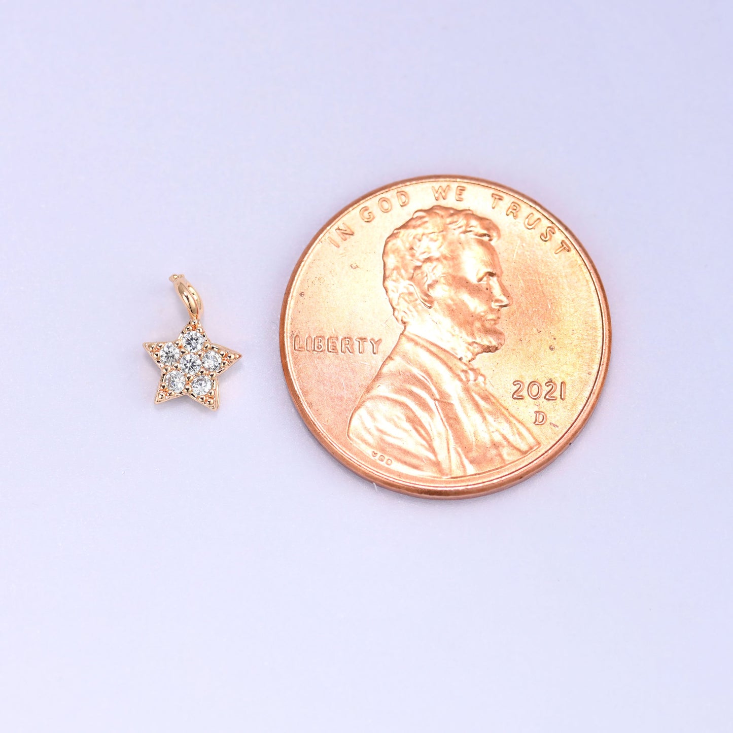 Small gold charms, one star charm shown beside a US penny for size