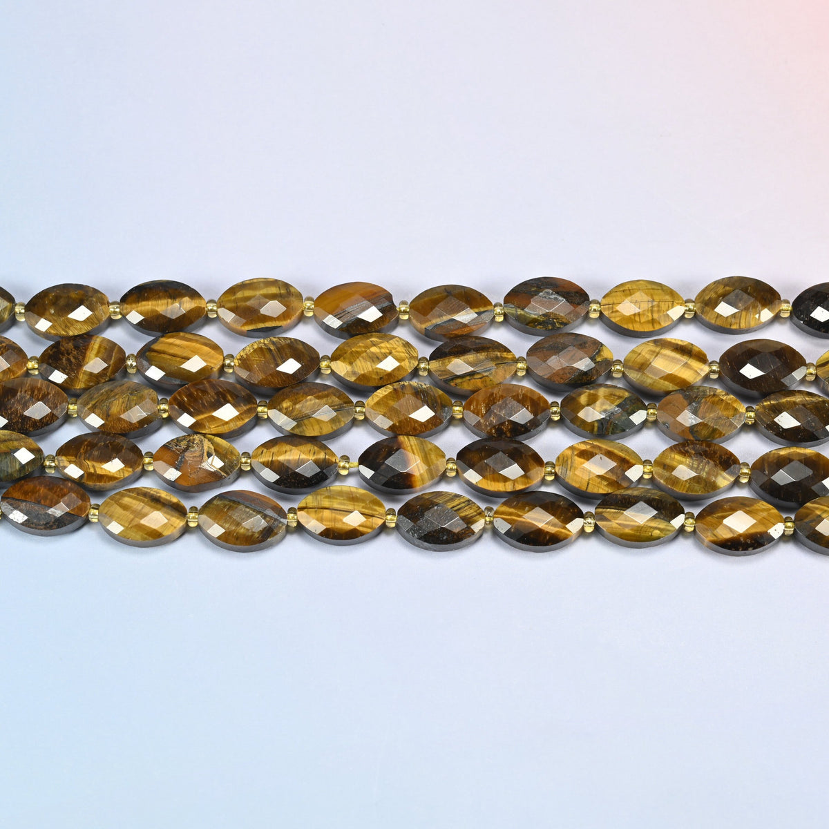 Several strands of tiger eye faceted flat oval beads laid in straight rows with gold seed bead spacers