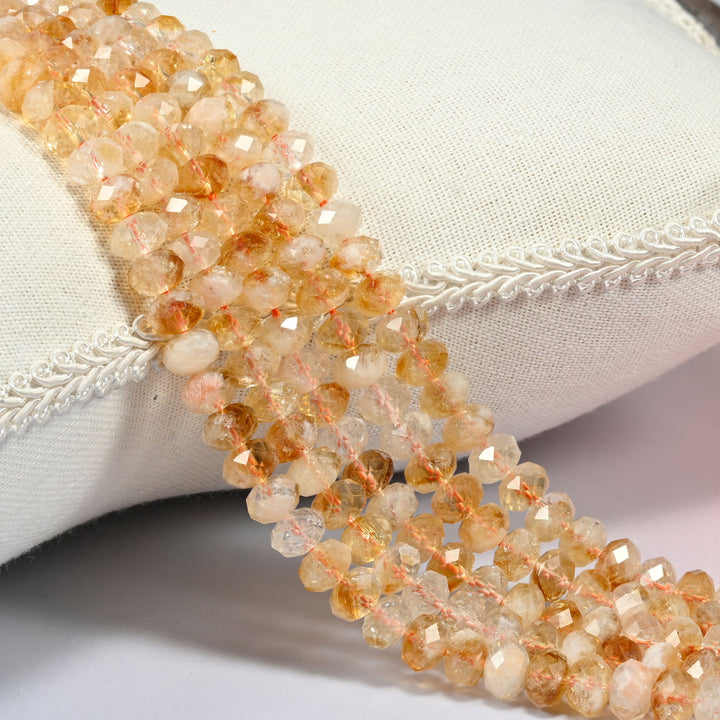 Citrine faceted rondelle beads 5x8mm in golden yellow, cream and honey orange, several strands draped over a white cushion