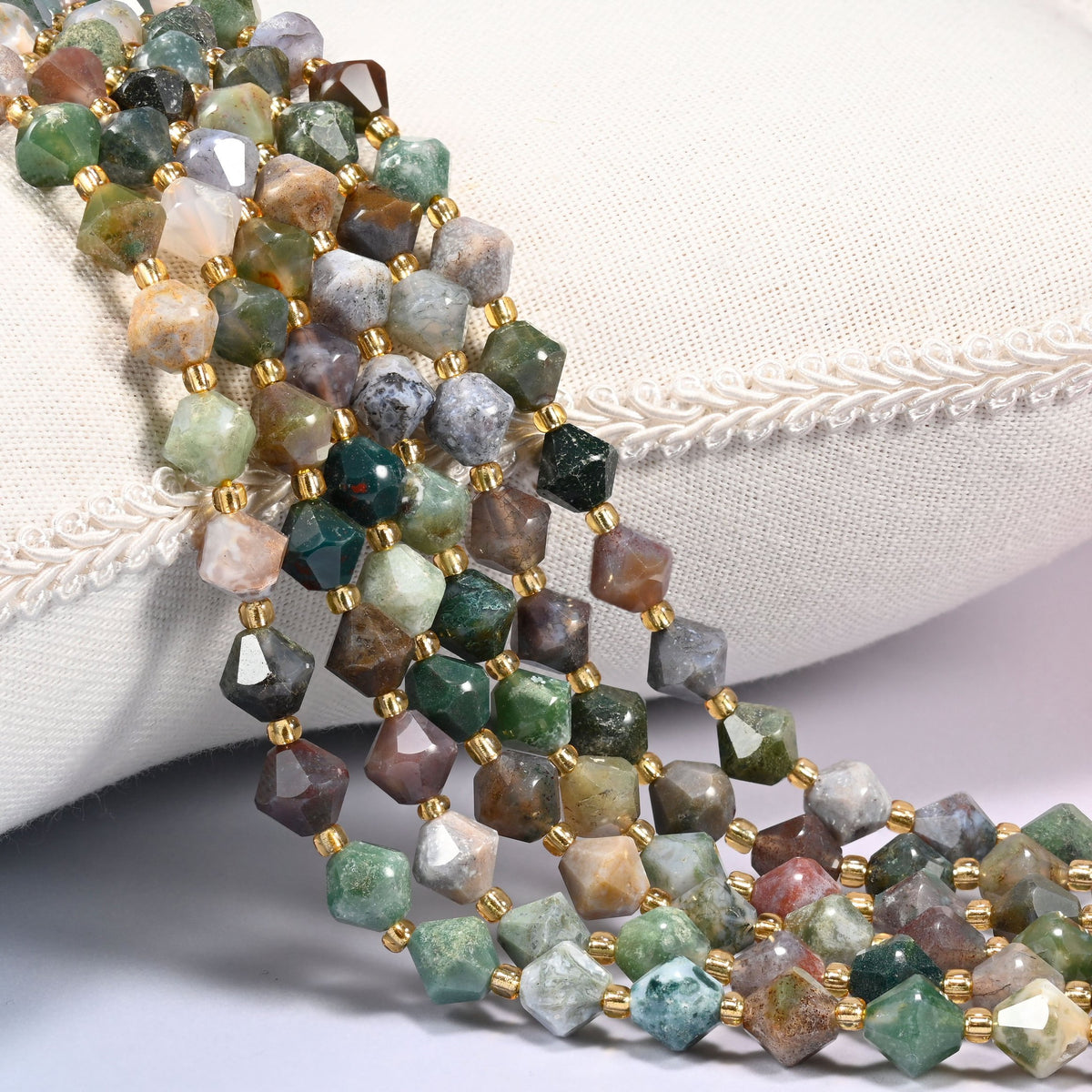Indian Agate faceted bicone beads 8mm with gold-tone spacers, strand draped over a woven cushion trim