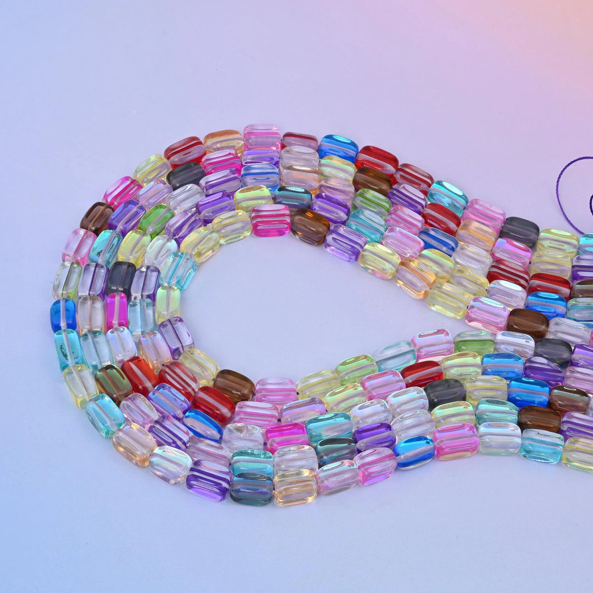 Rainbow mystic aura rectangle glass beads laid in a long loop, every bead a different translucent colour with an iridescent finish.