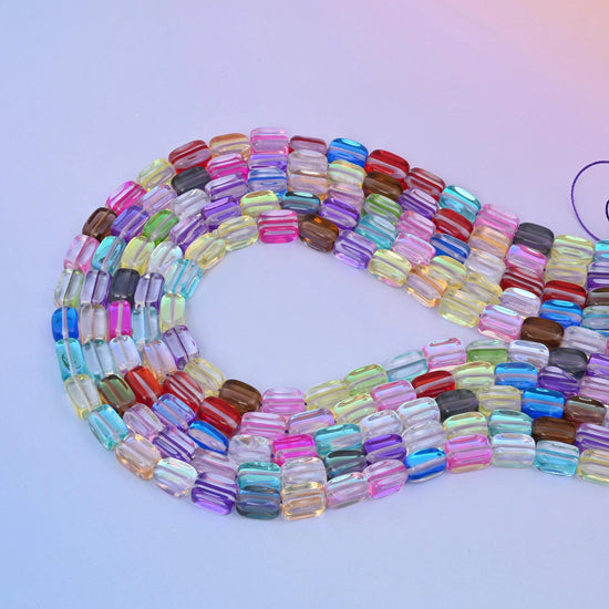 Rainbow mystic aura rectangle glass beads laid in a long loop, every bead a different translucent colour with an iridescent finish.