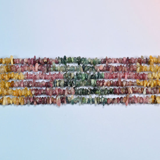 Several strands of multicolor tourmaline chip beads laid in straight rows, pink, green and golden yellow sections