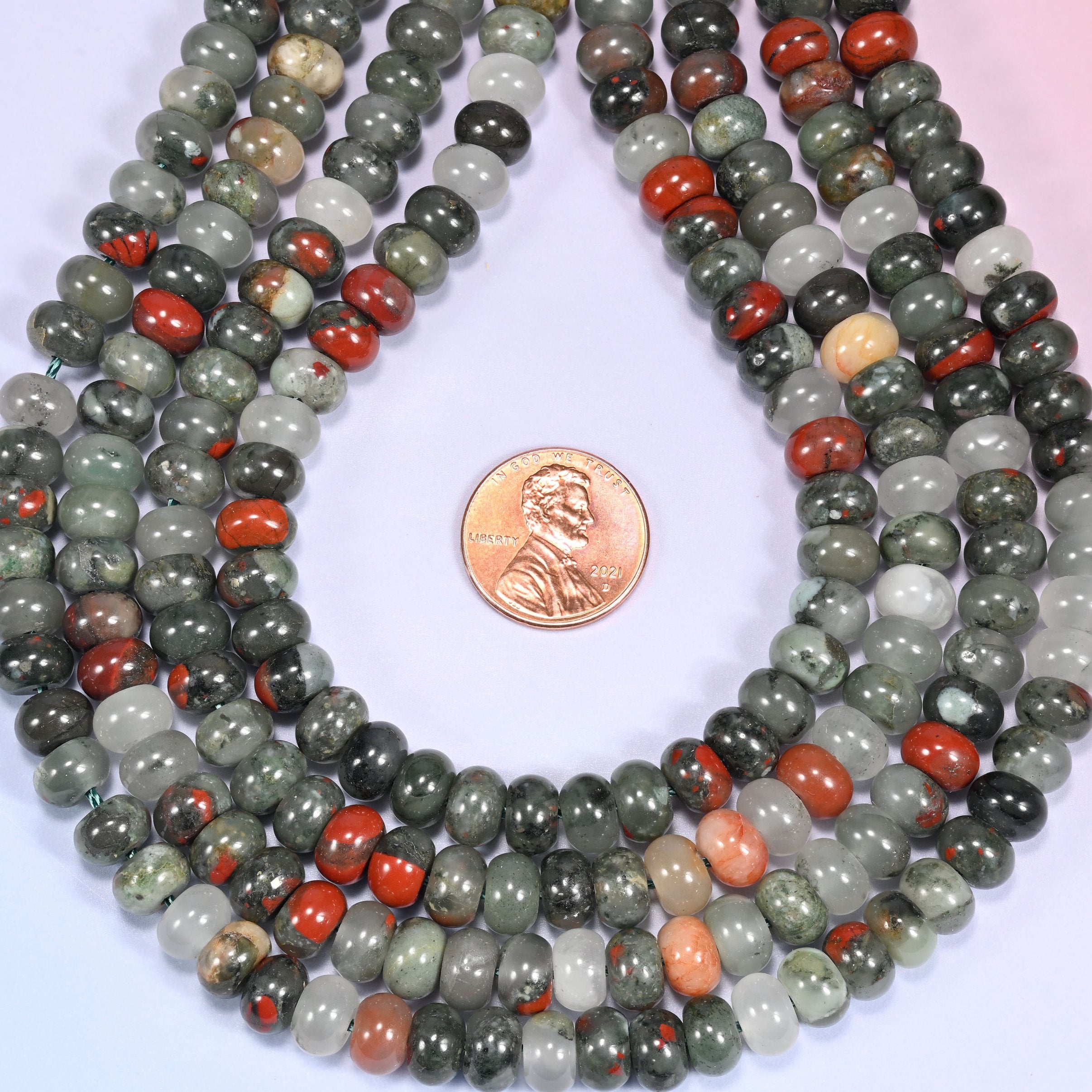 Bundled coil of African Bloodstone round beads on a lavender background with a penny placed at the center for scale.
