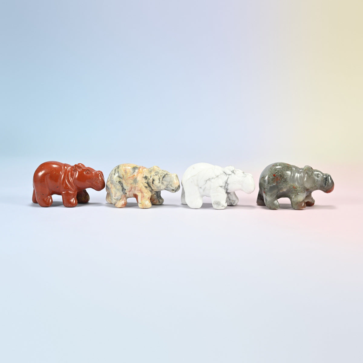 Four hippo carvings in red, cream, white and gray-green natural stone facing right