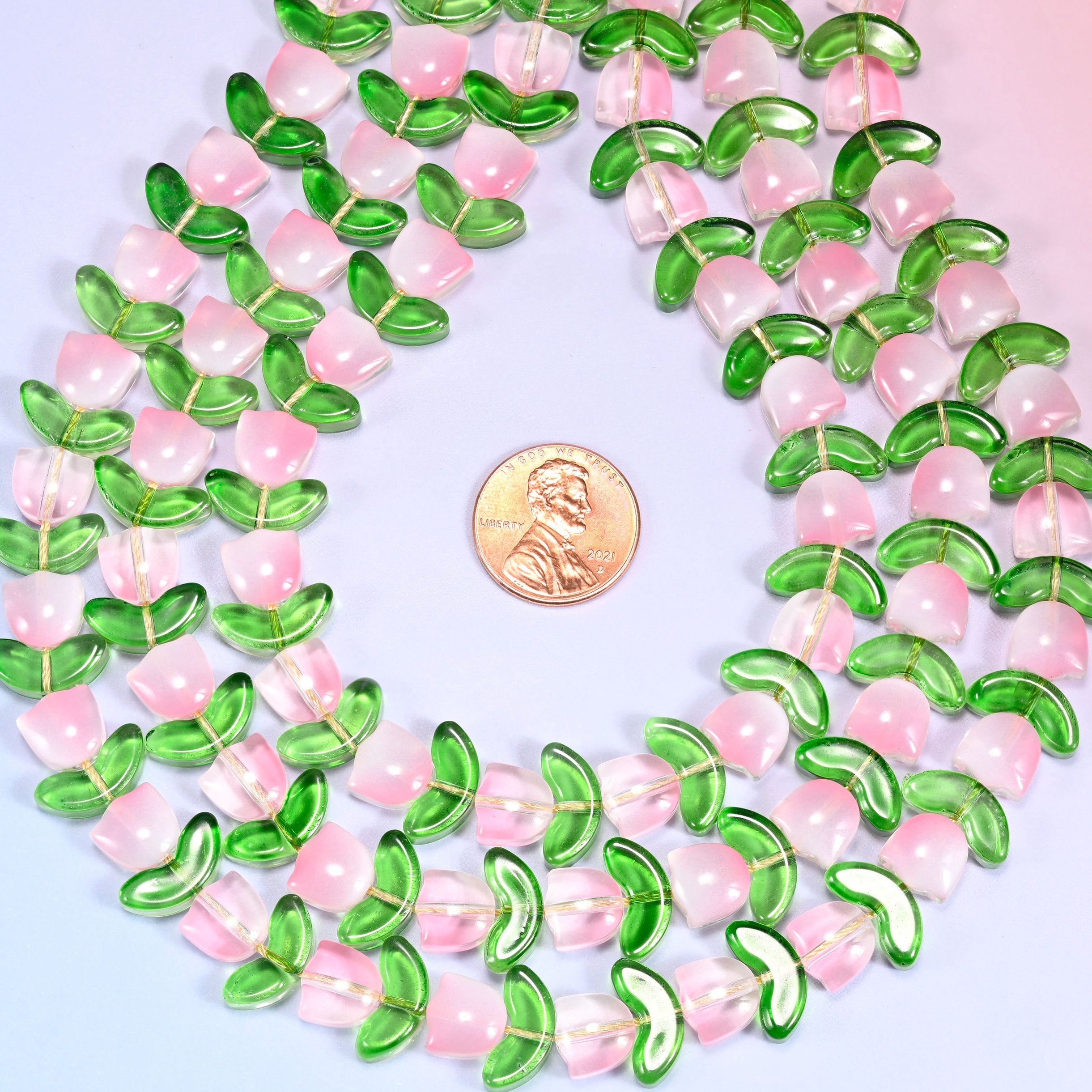 Wide view of a circular coil of pink tulip and green leaf glass bead strands on a lavender background.