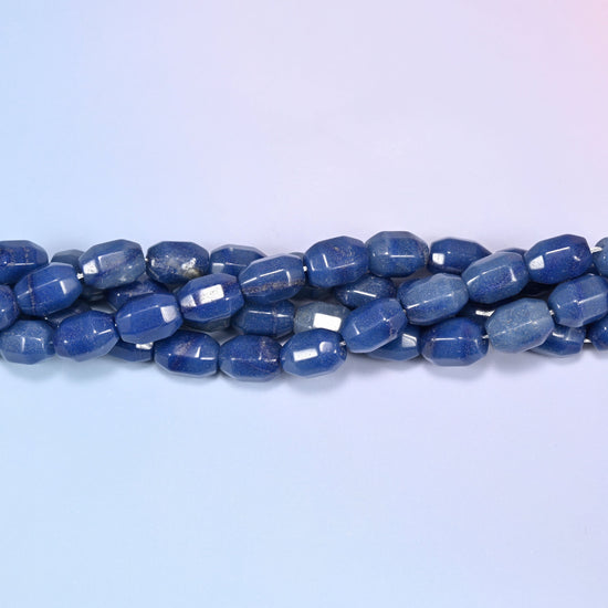 Horizontal row of blue faceted Aventurine barrel beads laid straight across a light blue and lavender gradient background.
