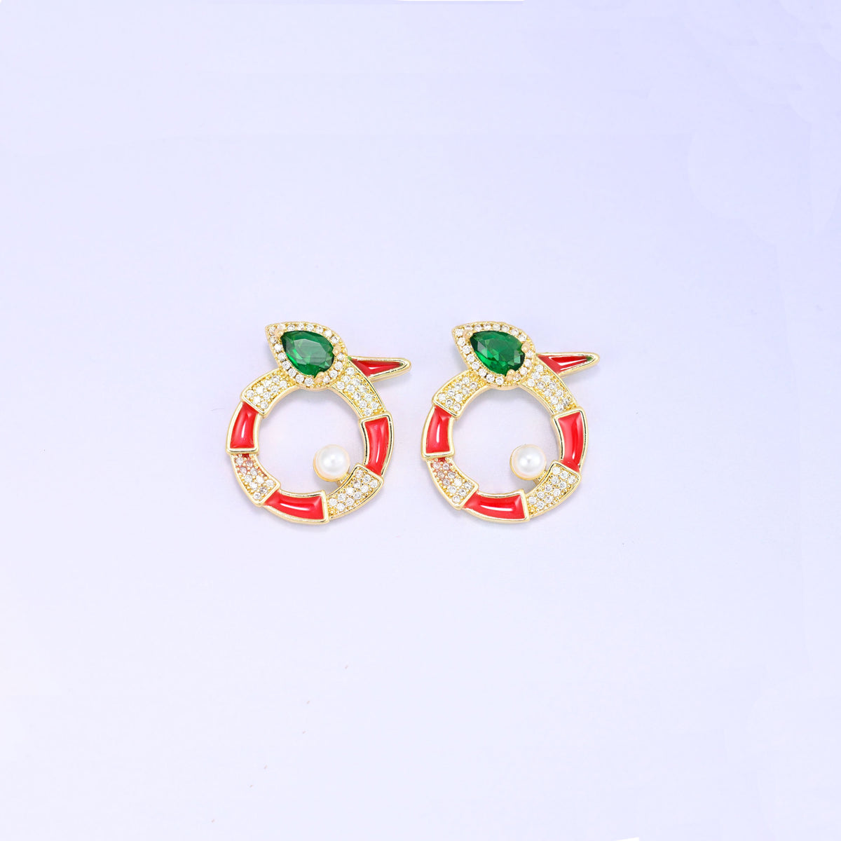 Two red round snake charms side by side, each 18K gold plated with a green pear cut stone head, zircon pave along the coil and a round pearl.